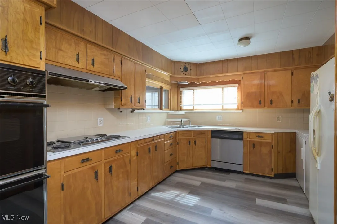 Kitchen featuring appliances with stainless steel finishes, light countertops, dark wood-type flooring, brown cabinetry, and backsplash