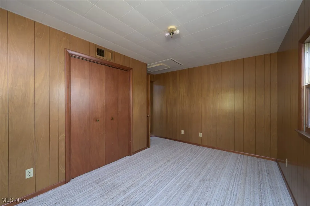 Unfurnished bedroom with wood walls, light colored carpet, a closet, and attic access
