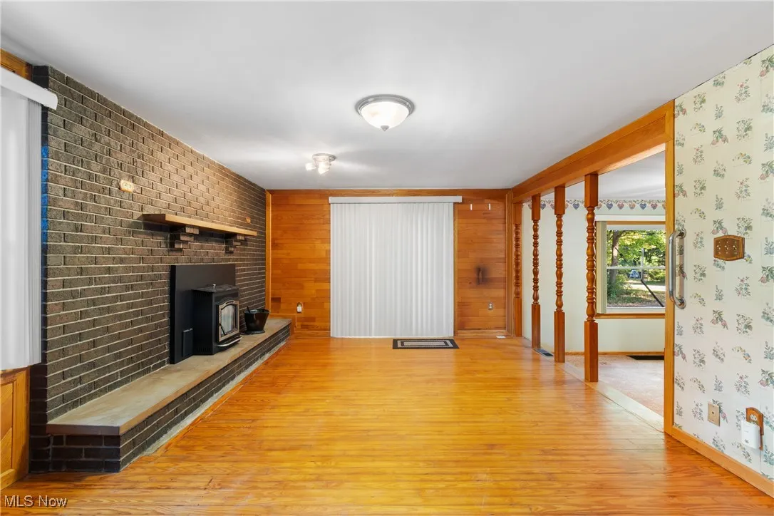 Unfurnished living room with light wood-style flooring, a wood stove, and wood walls