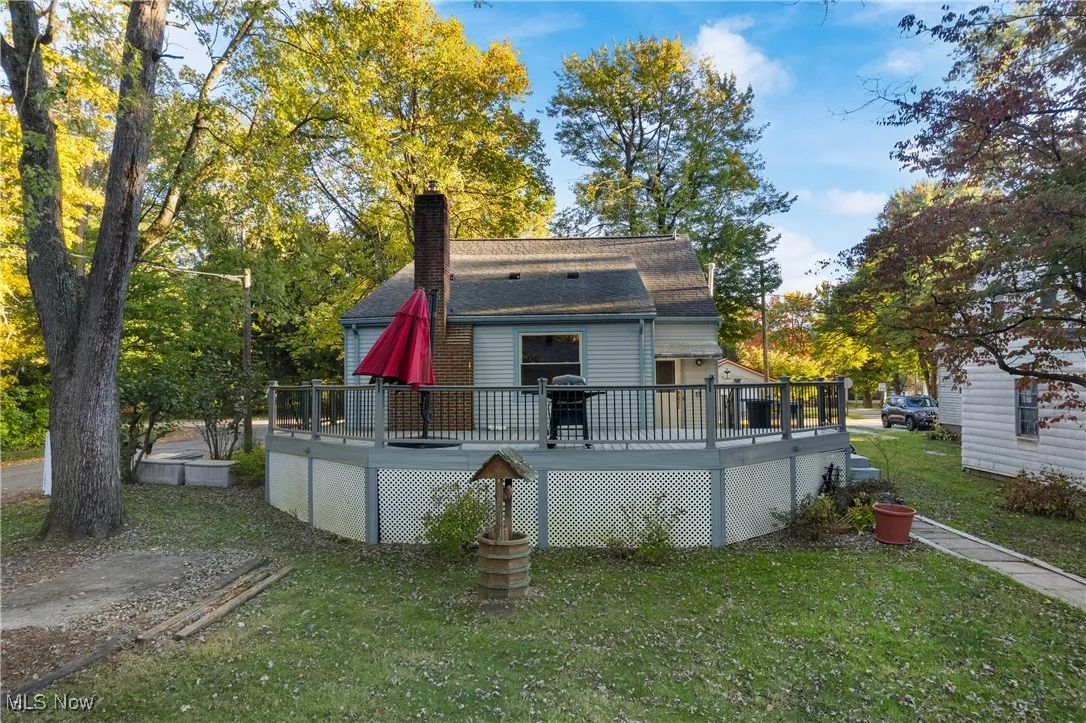 Rear view of house with a chimney, a yard, a wooden deck, a shingled roof, and view of wooded area