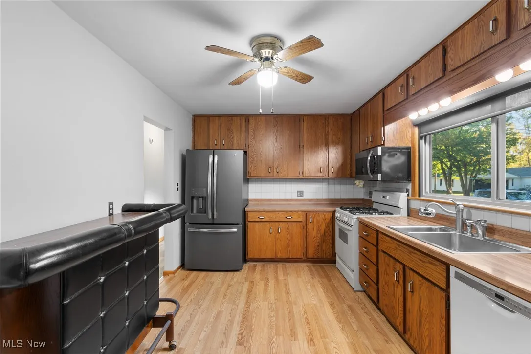 Kitchen featuring backsplash, stainless steel appliances, light wood finished floors, brown cabinets, and ceiling fan