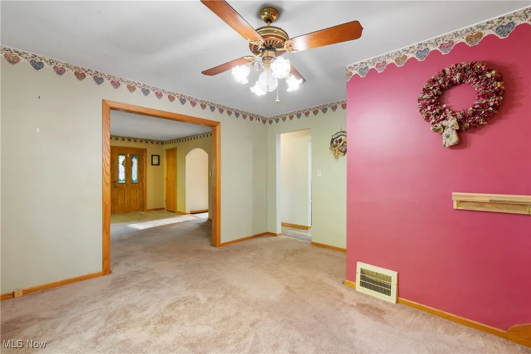 Unfurnished room with light colored carpet, arched walkways, and a ceiling fan