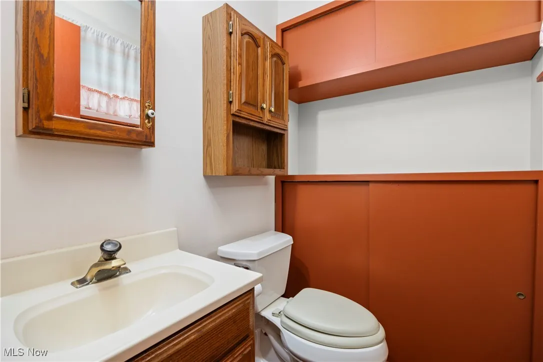 Half bathroom featuring vanity and toilet and shelving up and down entrance is from the primary bedroom