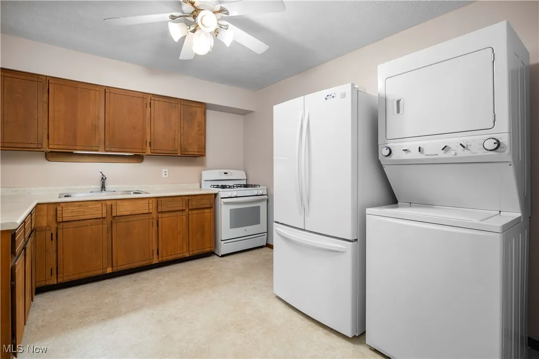 Kitchen with white appliances, light countertops, wood cabinetry, and ceiling fan
