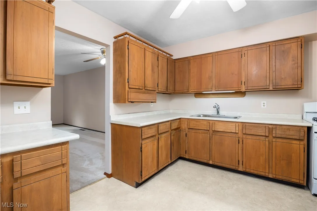 Kitchen with ceiling fan, light countertops, wood cabinetry, view facing the living room