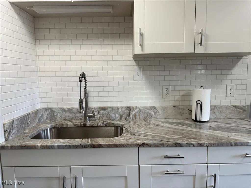 Kitchen with light stone countertops, white cabinets, and decorative backsplash