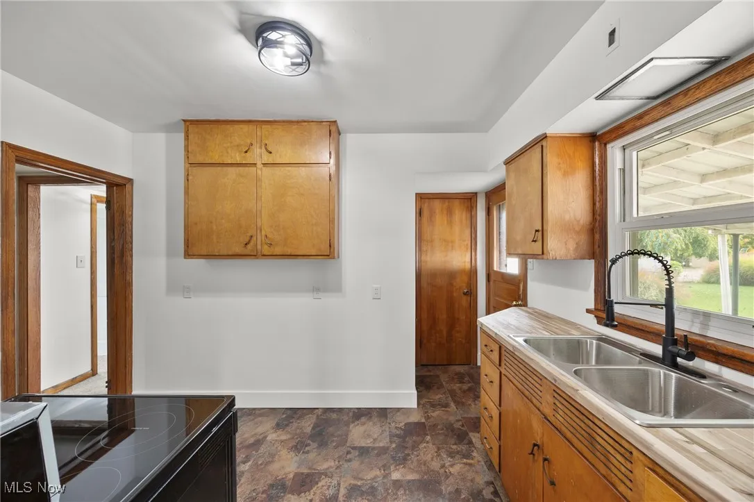 Kitchen featuring stone finish floors, brown cabinets, black range with electric stovetop, and light countertops
