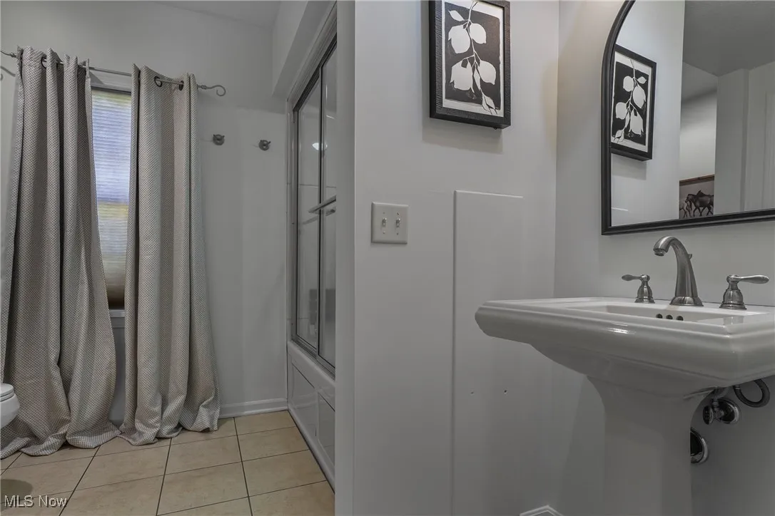 Full bath with light tile patterned floors and combined bath / shower with glass door