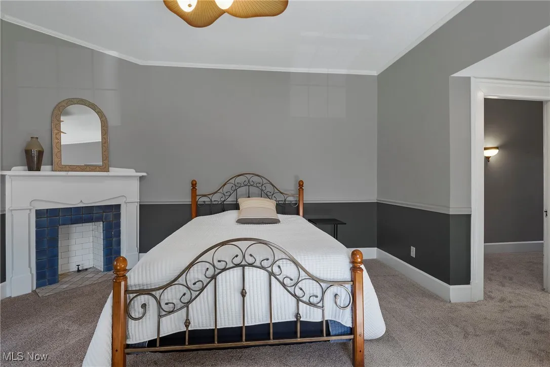 Carpeted bedroom with ornamental molding, ceiling fan, and a tiled fireplace