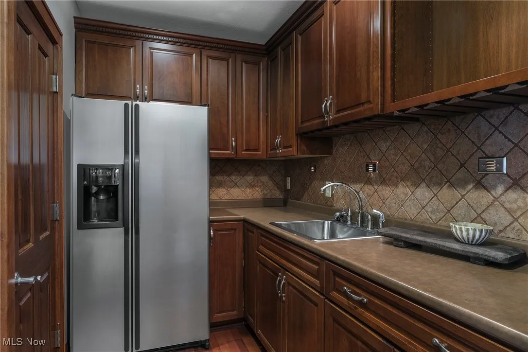 Kitchen with stainless steel refrigerator with ice dispenser, dark countertops, backsplash, dark brown cabinets, and dark wood finished floors
