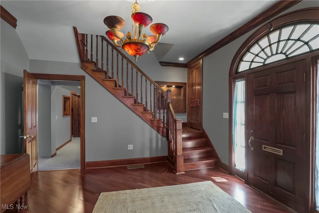 Foyer with dark wood-style flooring, crown molding, stairs, a chandelier, and recessed lighting