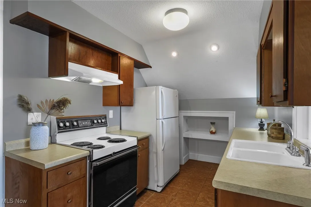 Kitchen featuring open shelves, electric range oven, lofted ceiling, a textured ceiling, and light countertops
