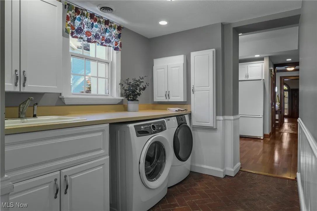 Washroom with brick flooring, washing machine and clothes dryer, cabinet space, and recessed lighting