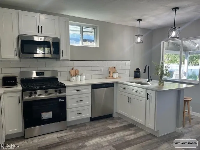 Kitchen with a peninsula, stainless steel appliances, white cabinets, tasteful backsplash, and hanging light fixtures