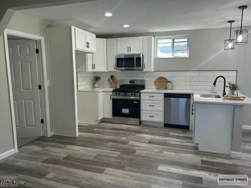 Kitchen with appliances with stainless steel finishes, backsplash, a peninsula, white cabinetry, and recessed lighting