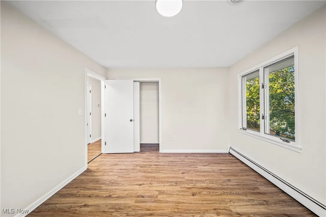Unfurnished bedroom with baseboard heating, a closet, and light wood-type flooring