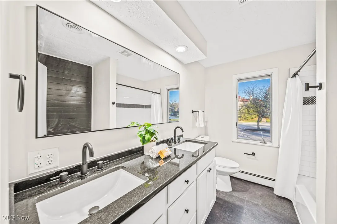 Full bathroom featuring toilet, vanity, shower / bath combination with curtain, and a baseboard heating unit