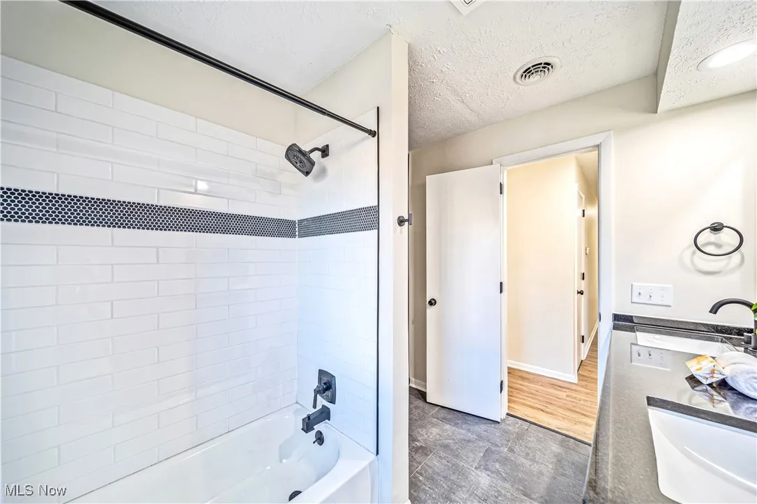 Bathroom with tiled shower / bath, vanity, wood-type flooring, and a textured ceiling