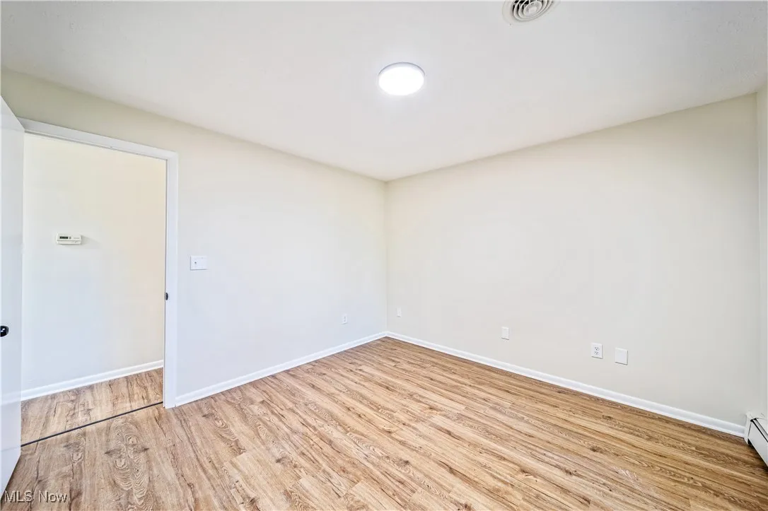 Empty room with a baseboard radiator and light hardwood / wood-style flooring