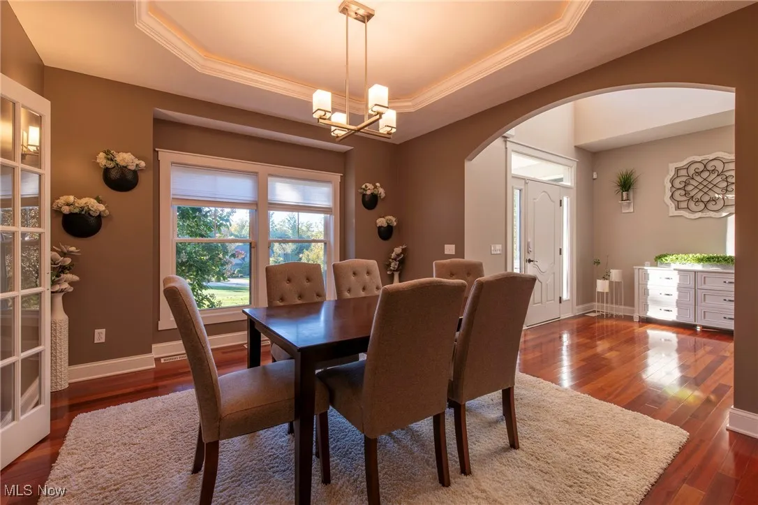 Dining room with a raised ceiling, dark wood finished floors, arched walkways, a chandelier, and ornamental molding