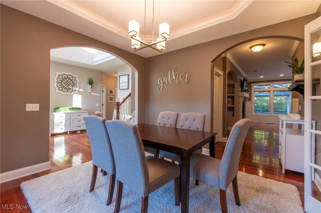 Dining space with ornamental molding, dark wood-style flooring, a tray ceiling, arched walkways, and stairway