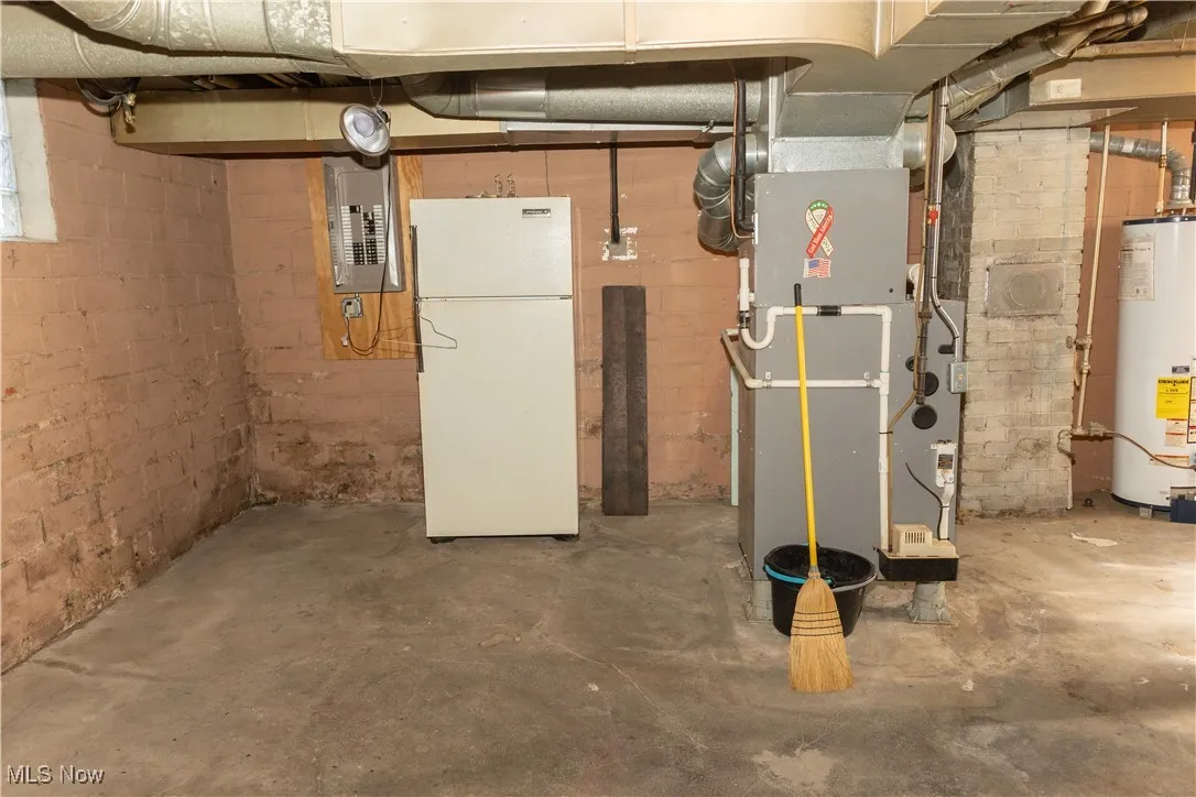 Basement with freestanding refrigerator, water heater, electric panel, and heating unit