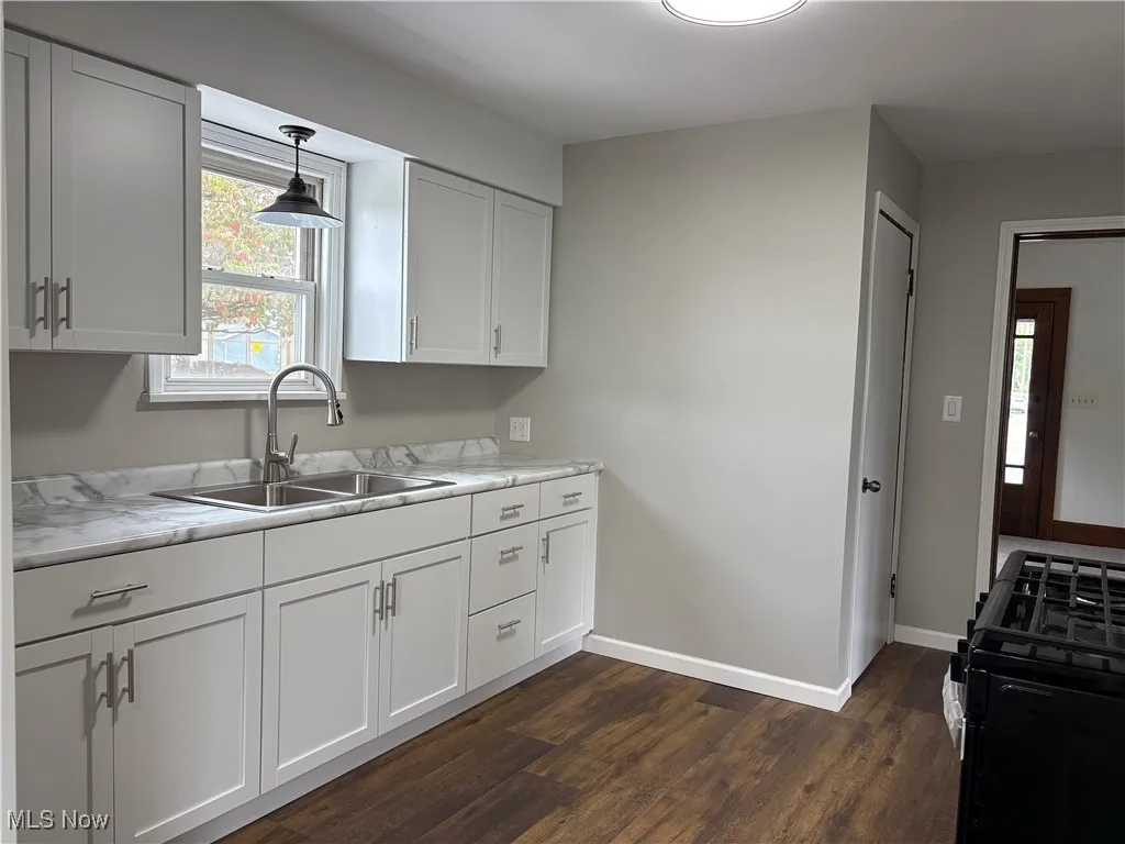 Kitchen featuring white cabinetry, black gas range, light countertops, dark wood finished floors, and hanging light fixtures