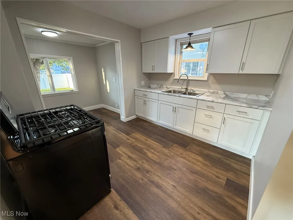 Kitchen featuring black gas range oven, white cabinets, light countertops, dark wood-type flooring, and pendant lighting