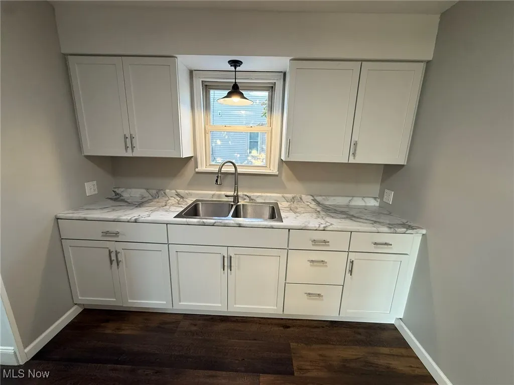 Kitchen featuring white cabinets, dark wood-style floors, pendant lighting, and light stone countertops