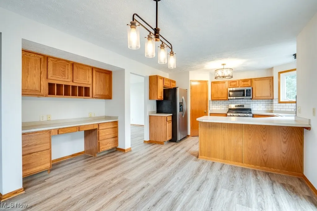 Kitchen with light countertops, a peninsula, backsplash, decorative light fixtures, and stainless steel appliances