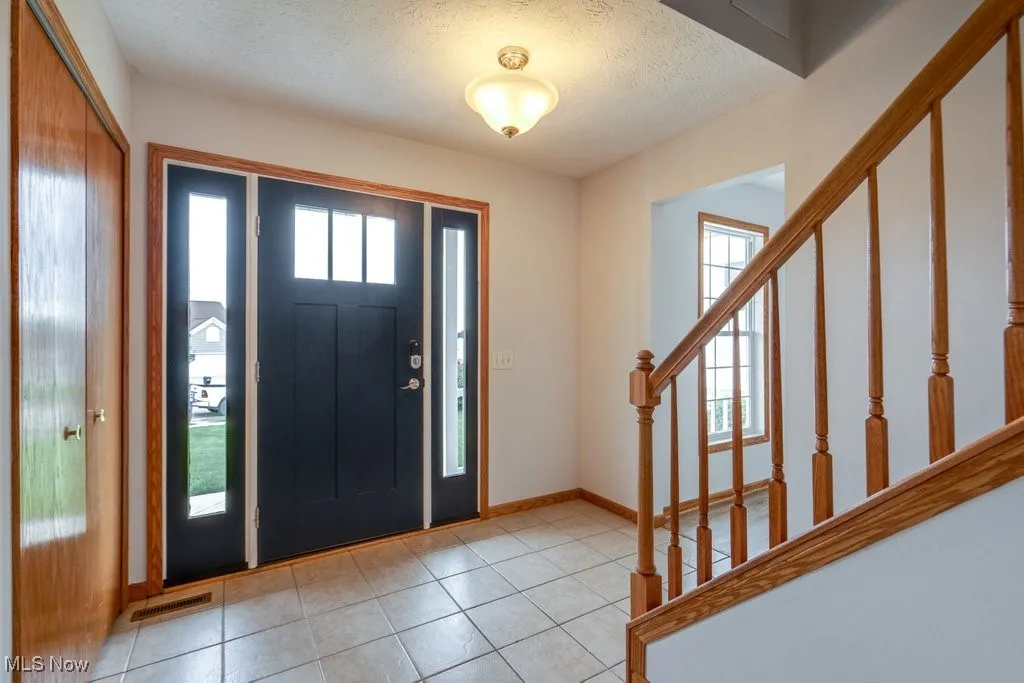 Foyer entrance featuring a textured ceiling, healthy amount of natural light, light tile patterned flooring, and stairway