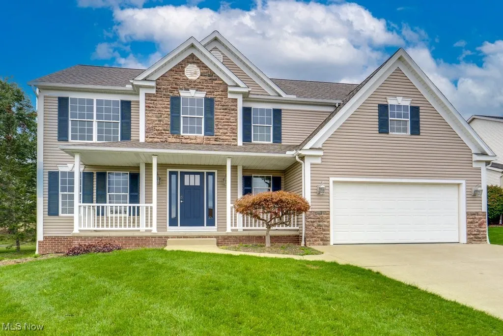 View of front of home with a porch, a front yard, concrete driveway, stone siding, and a garage