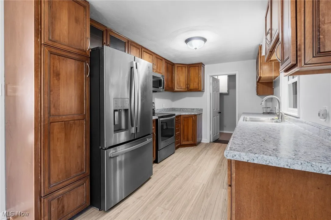 Kitchen featuring appliances with stainless steel finishes, brown cabinets, light countertops, and light wood-style flooring