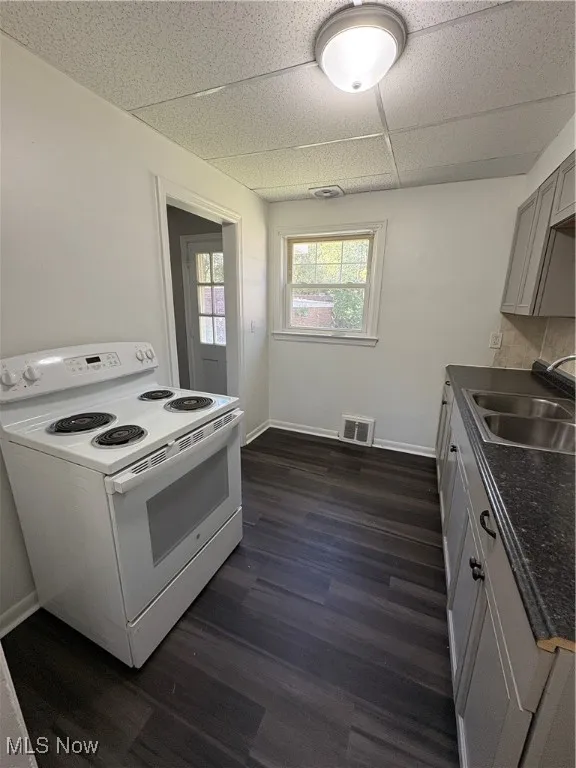 Kitchen featuring stove, dark countertops, dark wood-style flooring, a drop ceiling, and gray cabinetry