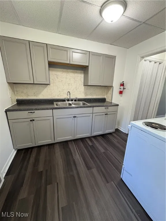 Kitchen featuring dark wood-type flooring, stove, gray cabinetry, dark countertops, and decorative backsplash