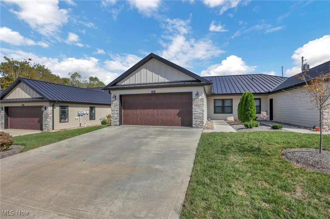 View of front of home with stone front, a metal roof, a garage, concrete driveway, and Diamond Kote siding