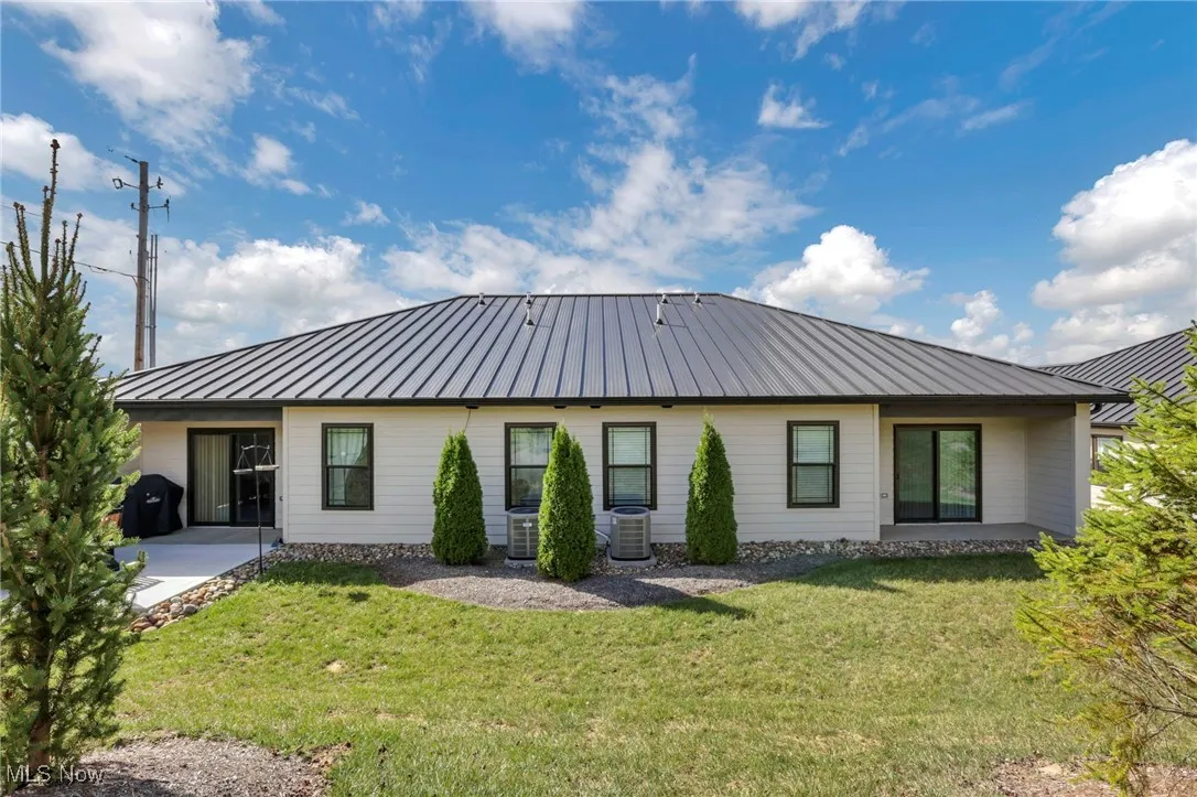 Rear view of property with a standing seam roof, a metal roof, a lawn, and a patio