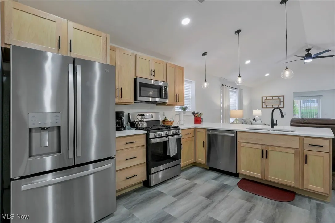 Kitchen featuring light brown cabinetry, stainless steel appliances, open floor plan, vaulted ceiling, and ceiling fan