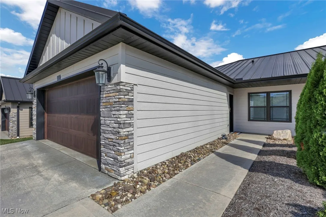 View of front of home with stone front, a metal roof, a garage, concrete driveway, and Diamond Kote siding
