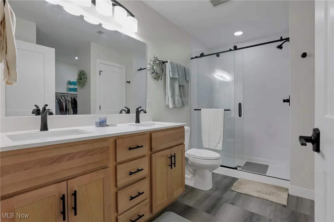 Bathroom featuring double vanity, a stall shower, a walk in closet, dark wood-type flooring, and recessed lighting