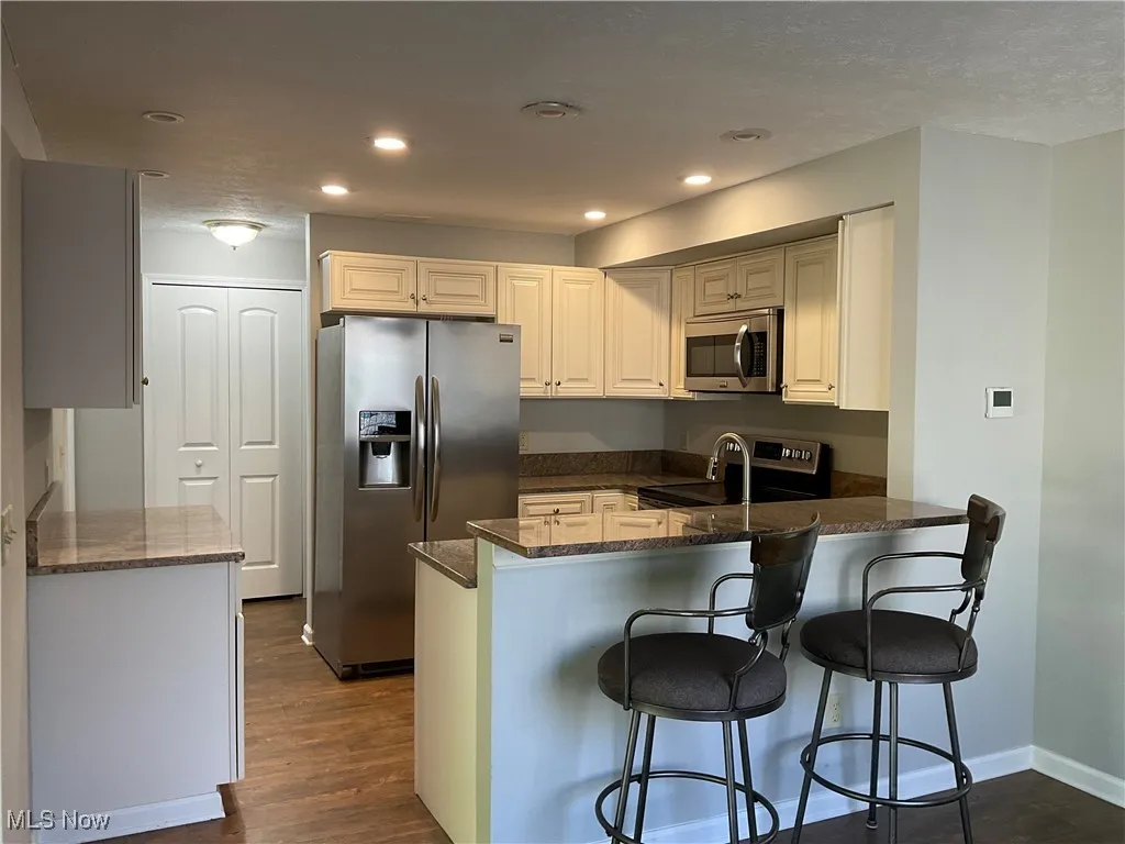 Kitchen with appliances with stainless steel finishes, a breakfast bar, dark wood-style flooring, dark stone countertops, and recessed lighting