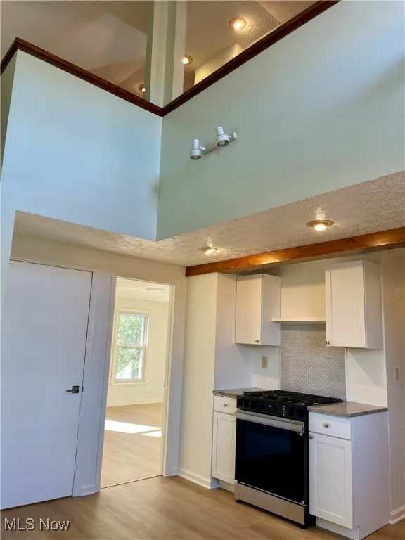 Kitchen featuring white cabinets, range with gas cooktop, tasteful backsplash, light wood-style flooring, and recessed lighting