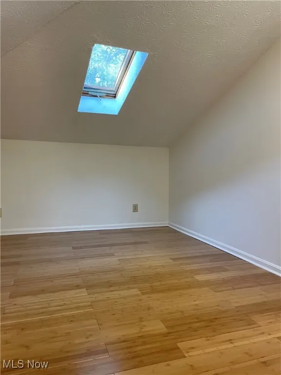 Bonus room featuring light wood-style flooring, a skylight, a textured ceiling, and vaulted ceiling