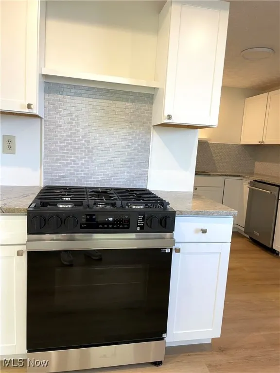 Kitchen with gas stove, backsplash, white cabinets, and light wood-style floors