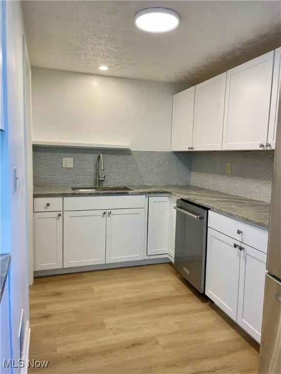 Kitchen featuring white cabinets, a textured ceiling, dark stone counters, light wood-style flooring, and stainless steel appliances