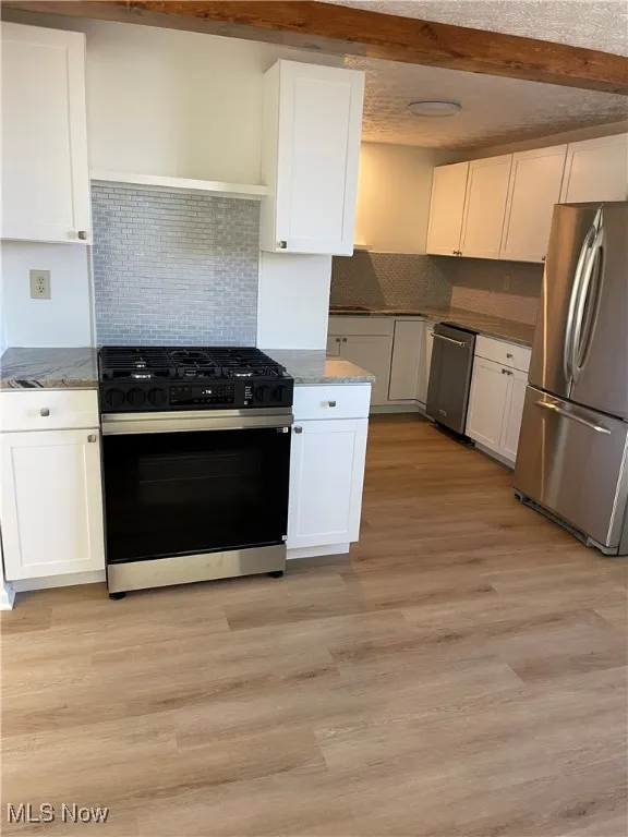 Kitchen with appliances with stainless steel finishes, decorative backsplash, white cabinets, light stone counters, and light wood-style floors