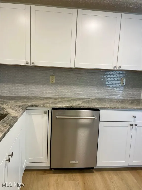Kitchen with decorative backsplash, dark stone counters, dishwasher, and white cabinetry