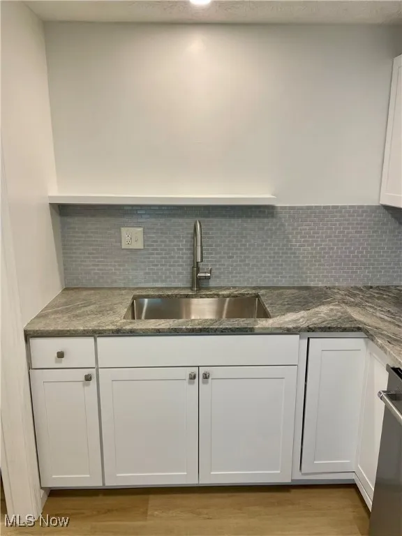 Kitchen with white cabinetry, backsplash, dark stone counters, a textured ceiling, and light wood-style flooring