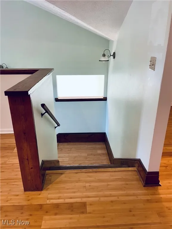 Stairs with hardwood / wood-style floors, lofted ceiling, and a textured ceiling