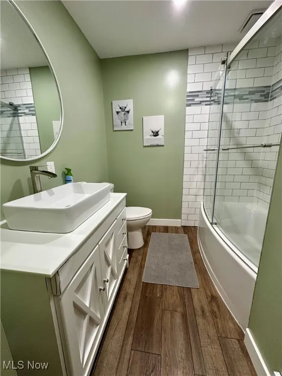 Bathroom featuring dark wood finished floors, bath / shower combo with glass door, and vanity